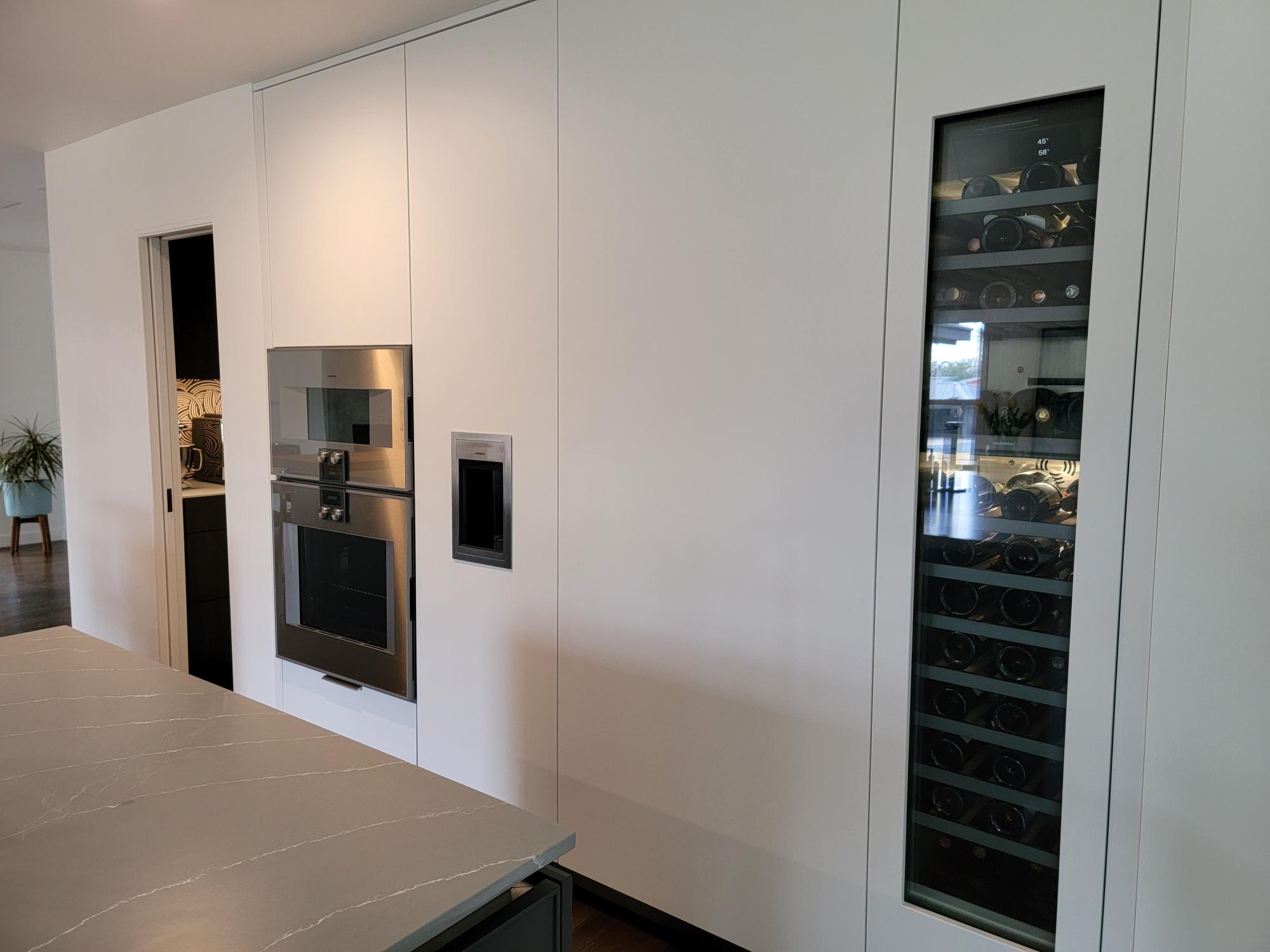 ultra-modern wall of tall white cabinets with integrated appliances and handle-less ovens