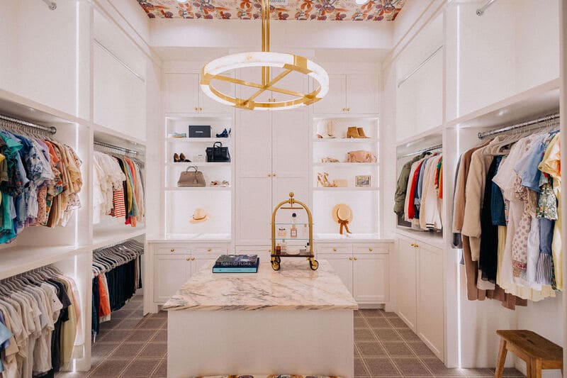 designer purse collection and hanging clothes in a luxury walk-in closet featuring a center island