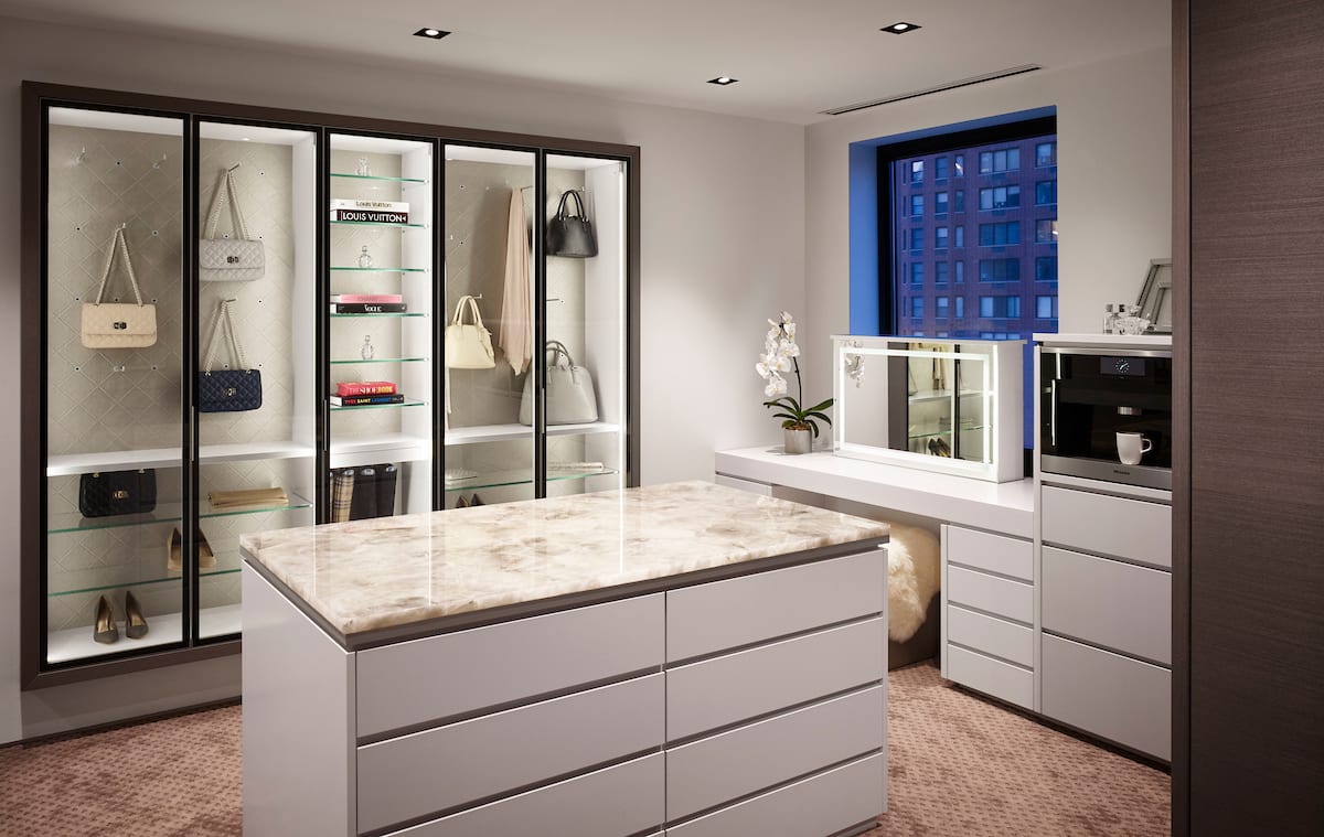 luxury wardrobe with glass-front cabinetry, custom dressing table, and island with storage drawers