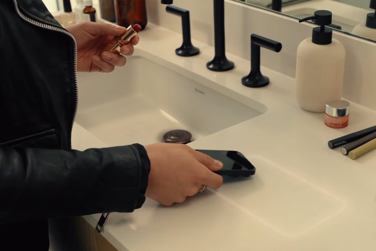 person placing phone to wirelessly chargie on freepower charging halo invisible device charger in a bath vanity