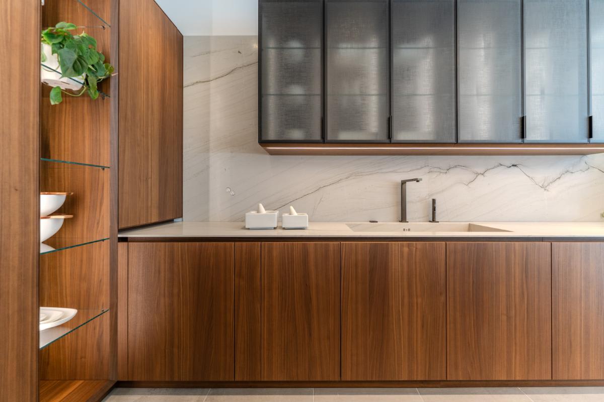 closeup of the upper cabinetry in a glance smoked glass finish above a wall of wood veneer cabinetry in the skywalk kitchen in the eggersmann la showroom
