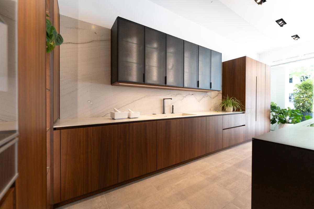 upper cabinetry in a glance smoked glass finish above a wall of wood veneer cabinetry in the skywalk kitchen in the eggersmann la showroom