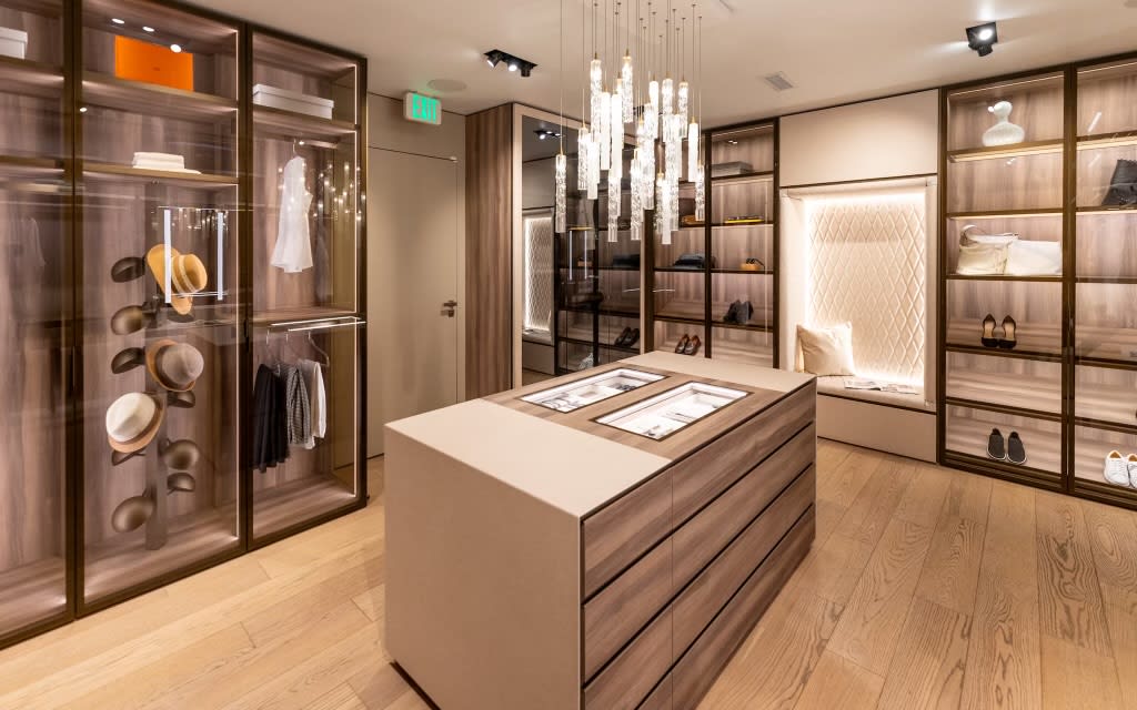 luxury walk-in wardrobe display with storage island, glass-front display storage, and tufted upholstered seating niche in the eggersmann la showroom