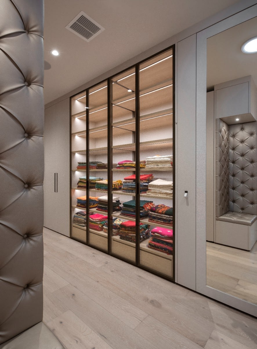 glass-front cabinetry and tufted-upholstered bench in a wardrobe designed by eggersmann scottsdale in a fulton ranch home