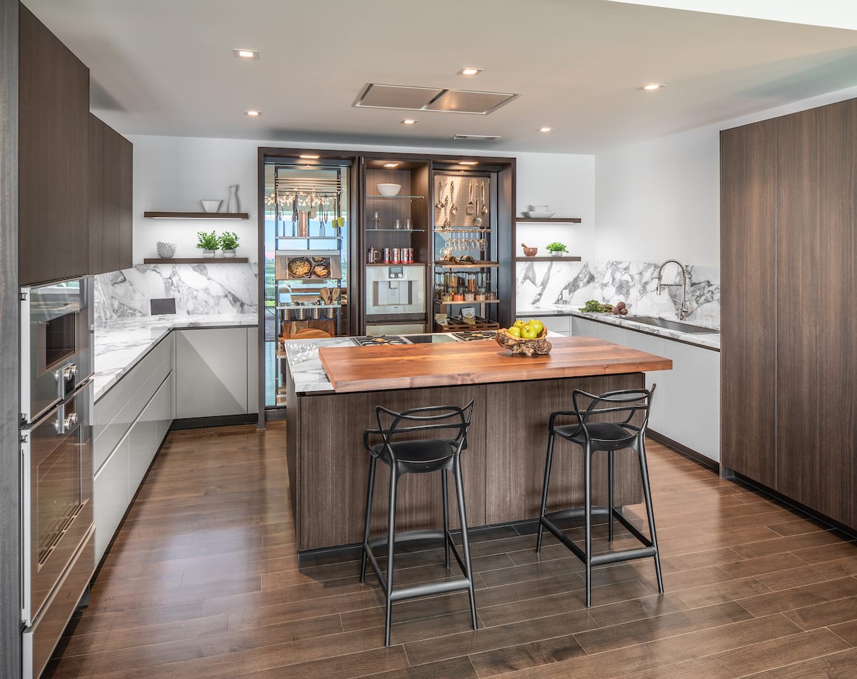 motion sliding countertop open in an island with bar seating in a modern eggersmann usa kitchen design featuring work's turnstile organizational system and lighted open shelving.