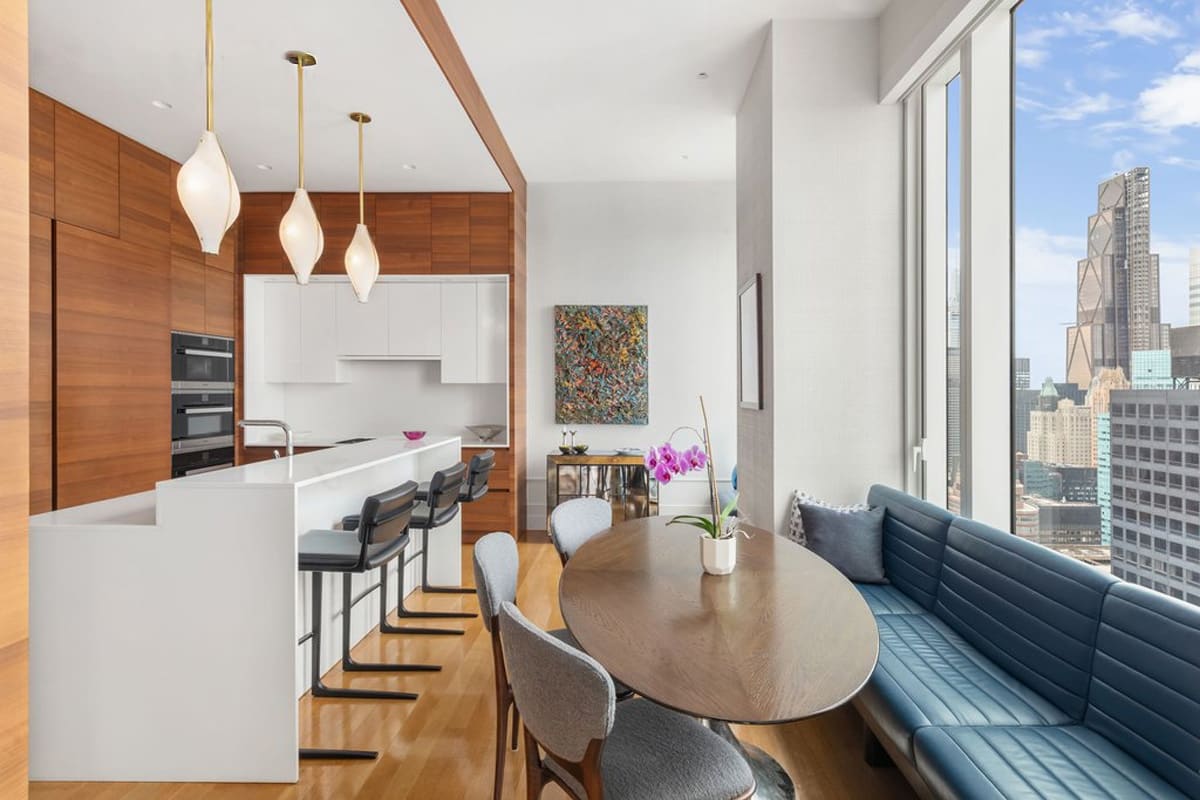 gloss white island and wood-veneered wall cabinetry of a kitchen and dining area with blue leather upholstered dining banquette designed by eggersmann residence in 252 east 57th st of nyc