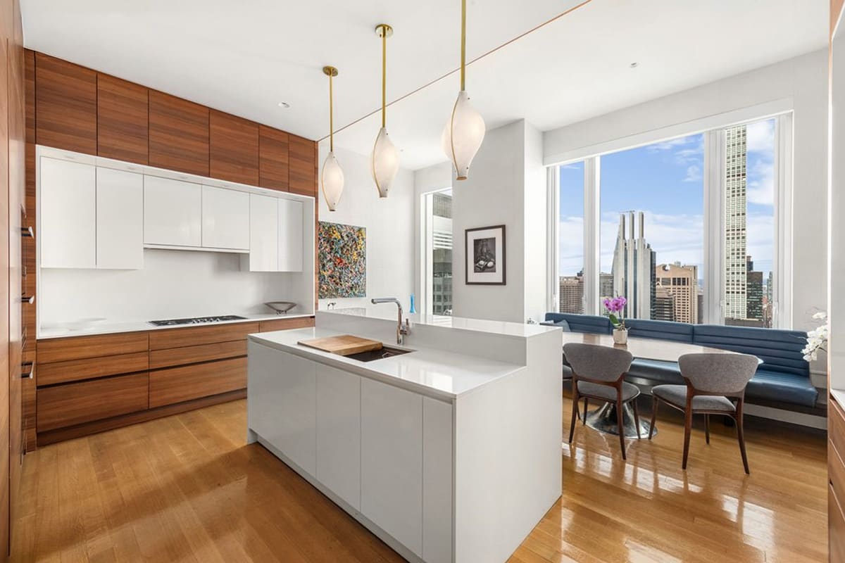 galley of gloss white island and wood-veneered wall cabinetry of a kitchen and dining area with blue leather upholstered dining banquette designed by eggersmann residence in 252 east 57th st of nyc