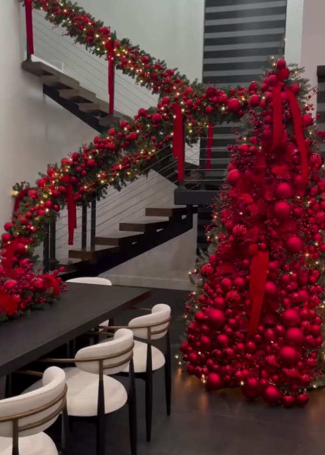 red-themed christmas tree in front of a red garland-draped staircase in a luxury home
