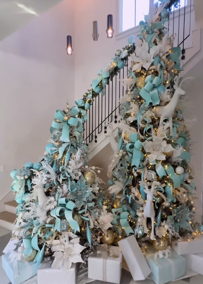 blue and white themed christmas tree in front of a blue and white garland-draped staircase in a luxury residence