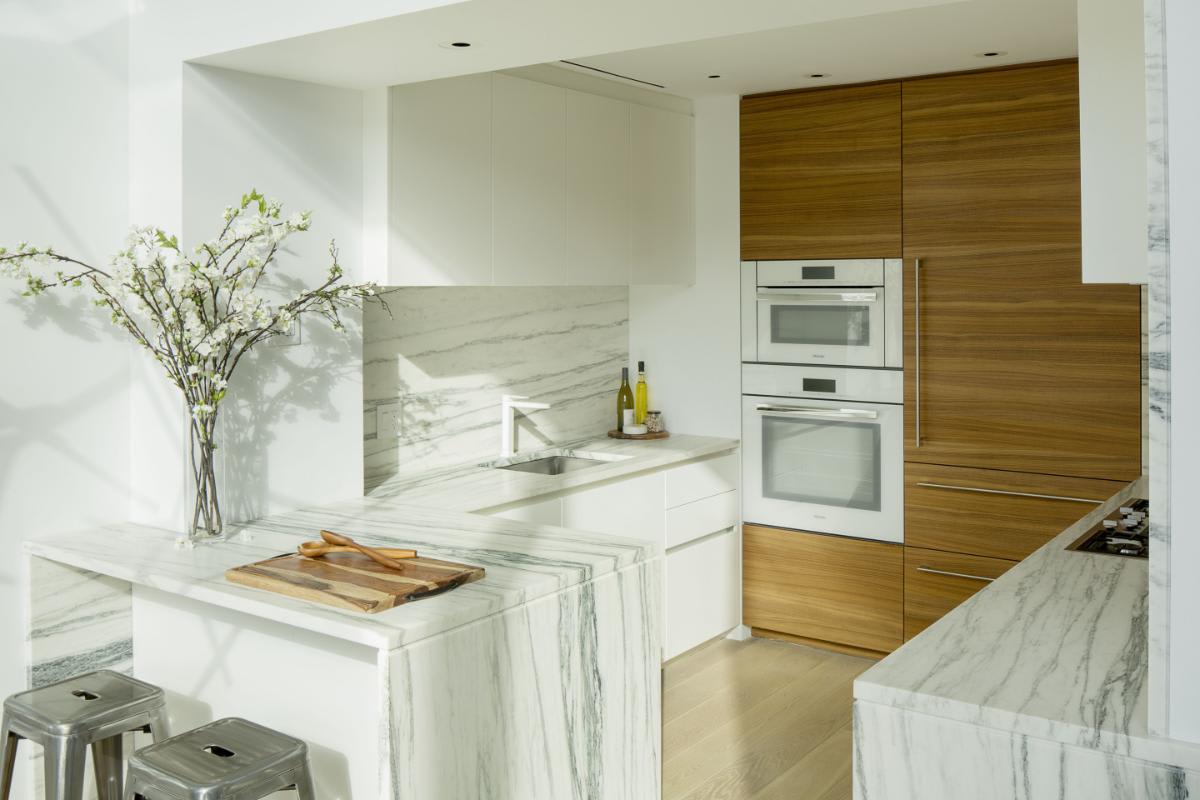 a luxury kitchen designed by eggersmann with calacutta marble counters and backsplashes with mid-tone wood veneer and white gloss finishes in a residence of chelsea waterside nyc