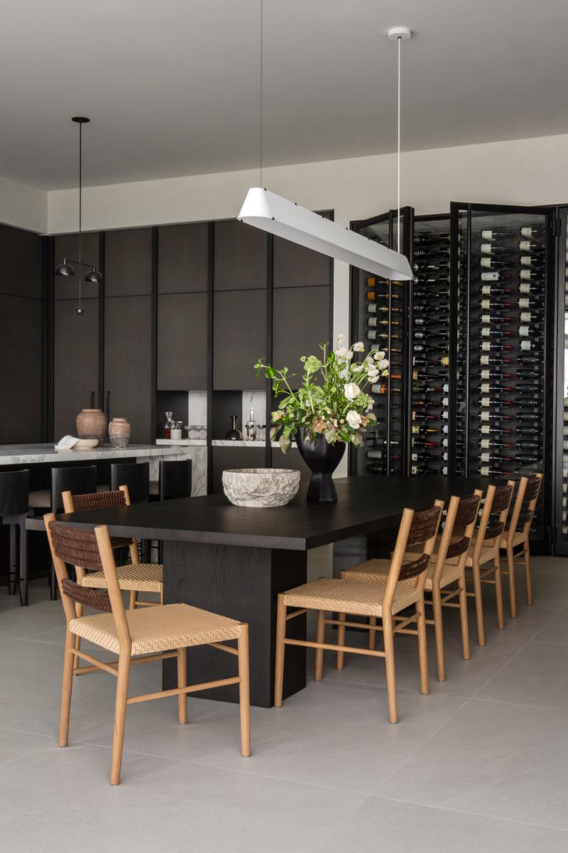 dining table with simple chairs in a lighter tone than the surrounding luxury kitchen's dark palette
