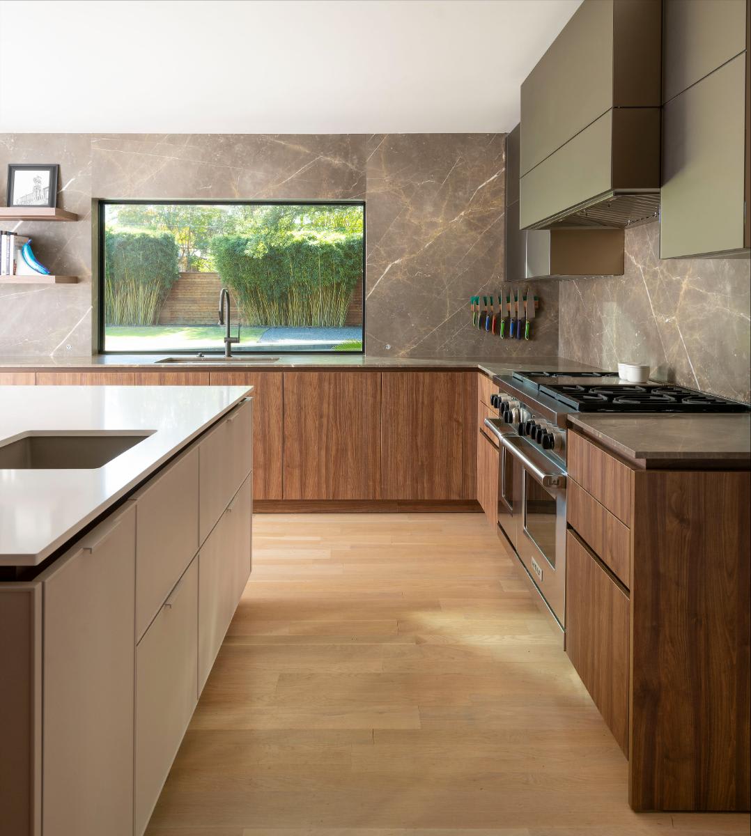 galley of a mid-century inspired kitchen designed by eggersmann for a Preston Hollow renovation looking out to a garden through a picture window over a sink with a gooseneck faucet