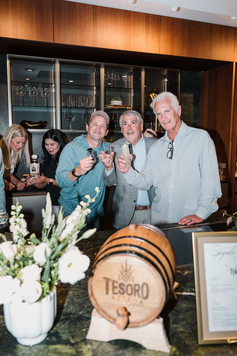 guests pose with tequila shots in front of tequila barrel at a tequila tasting event at the eggersmann laguna showroom