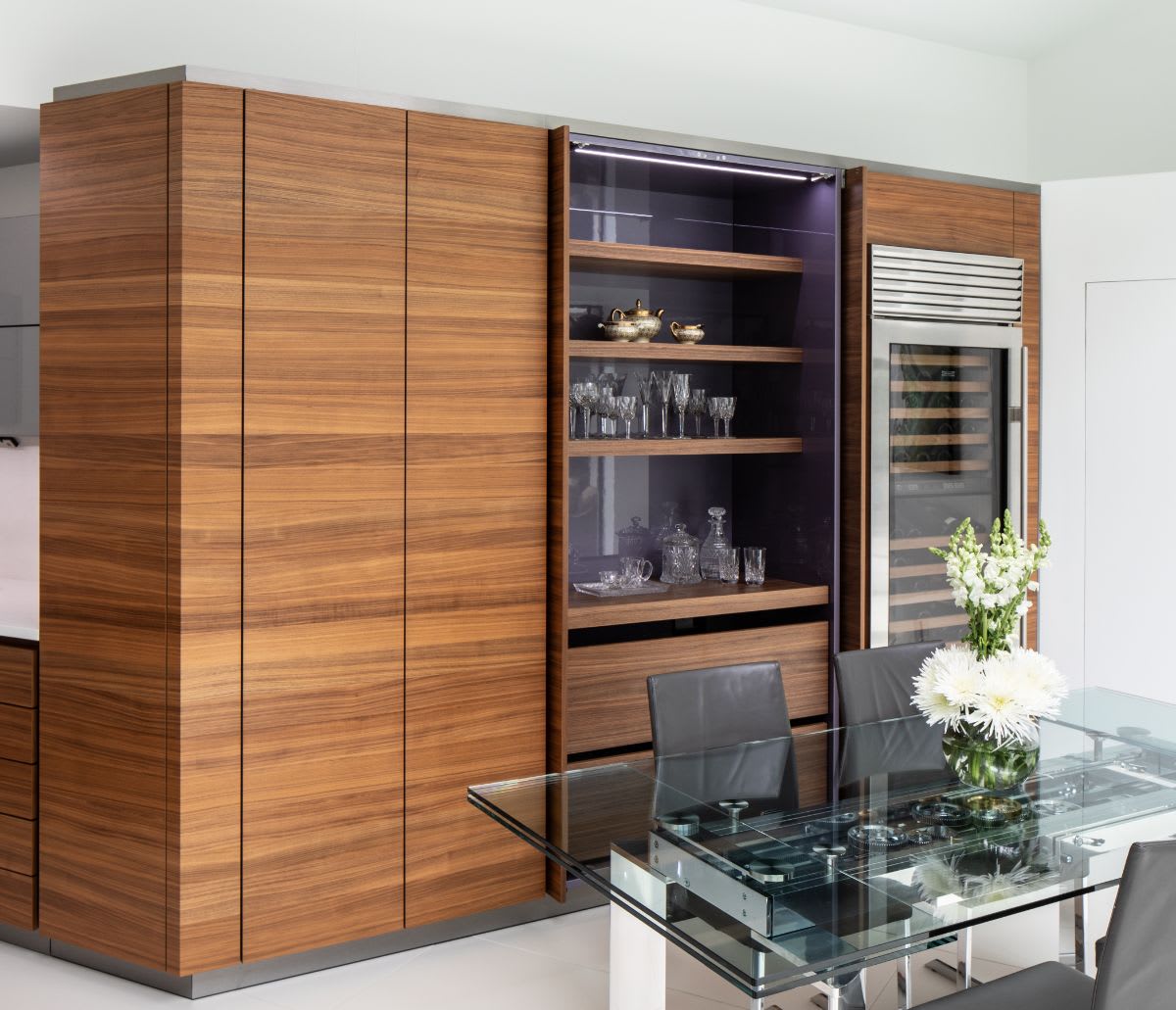 eggersmann designed horizontal-grained walnut cabinet wall featuring a hideaway bar area behind pocket doors that when opened reveal a very peri-colored shelf unit and drawer storage