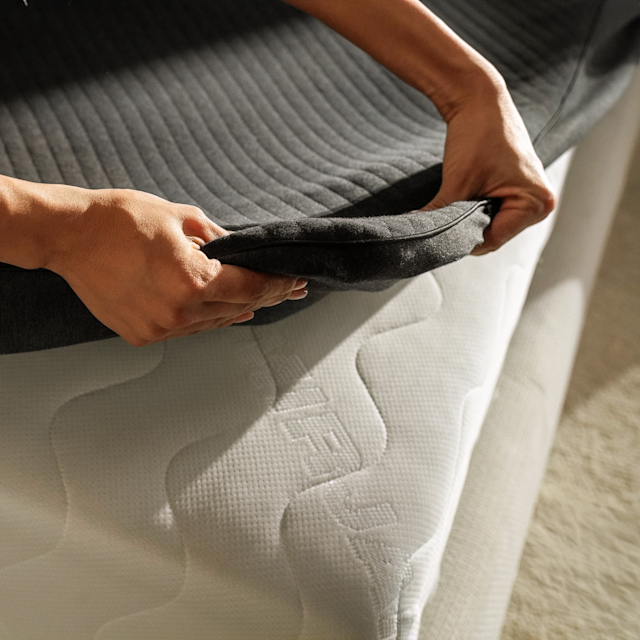 Hands fitting the Pod 6 Cover over the corner of a mattress.
