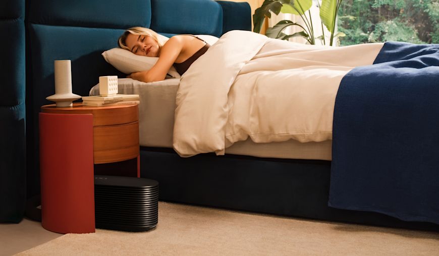 عضو في Eight Sleep نائم تحت لحاف، وجهاز Pod 6 Hub على الأرض بجانب السرير
