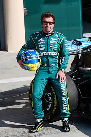 Fernando Alonso holding his helmet in the pit lane beside the Aston Martin car