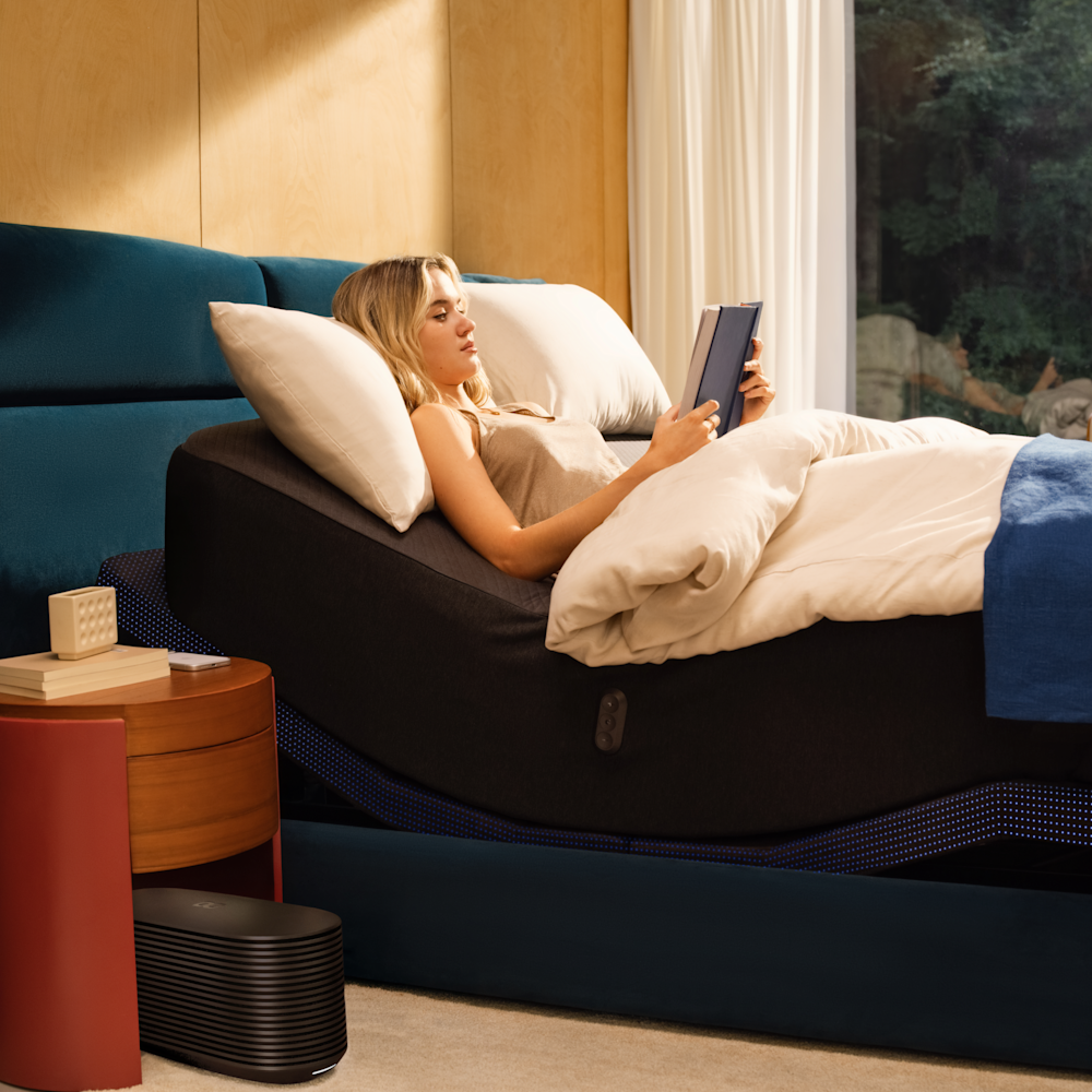 A woman reading in bed with the head raised, a lamp lit beside her.