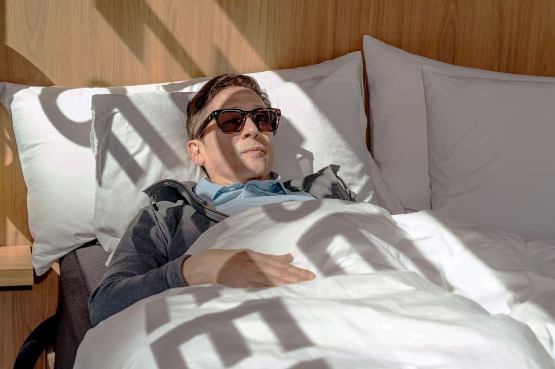 A guest in sunglasses relaxing under the covers of the Pod bed inside the House of Sleep truck