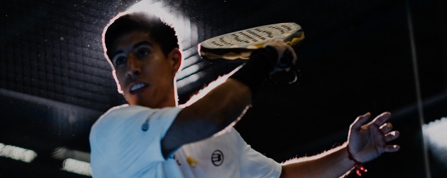 Federico Chingotto mid-swing on a padel court, wearing his Alpine F1 jersey, under stadium lights