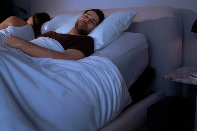 A couple asleep in a dark bedroom, one of them on their back