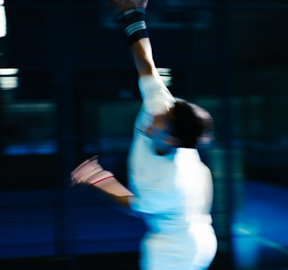 An athlete mid-serve, lit blue