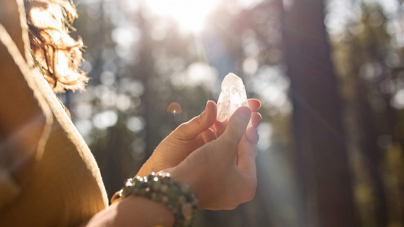 Kristall in Hand vor Waldhintergrund