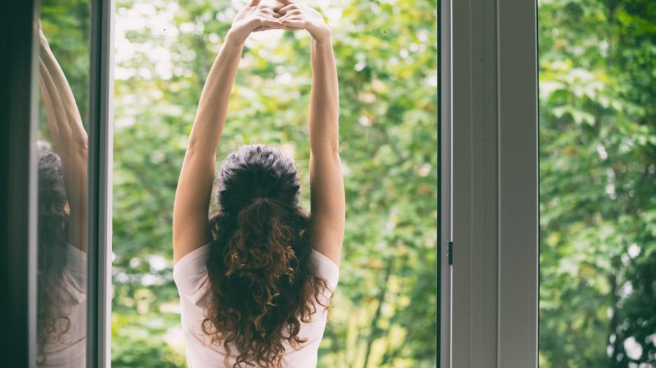 Frau etabliert Morgenroutine Frau streckt sich morgens vor dem Fenster