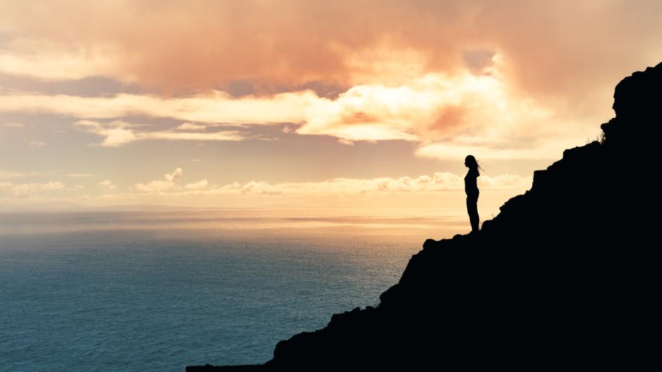 mental stärker werden frau steht auf felsen am meer im sonnenuntergang mental stärker werden frau steht auf felsen am meer im sonnenuntergang