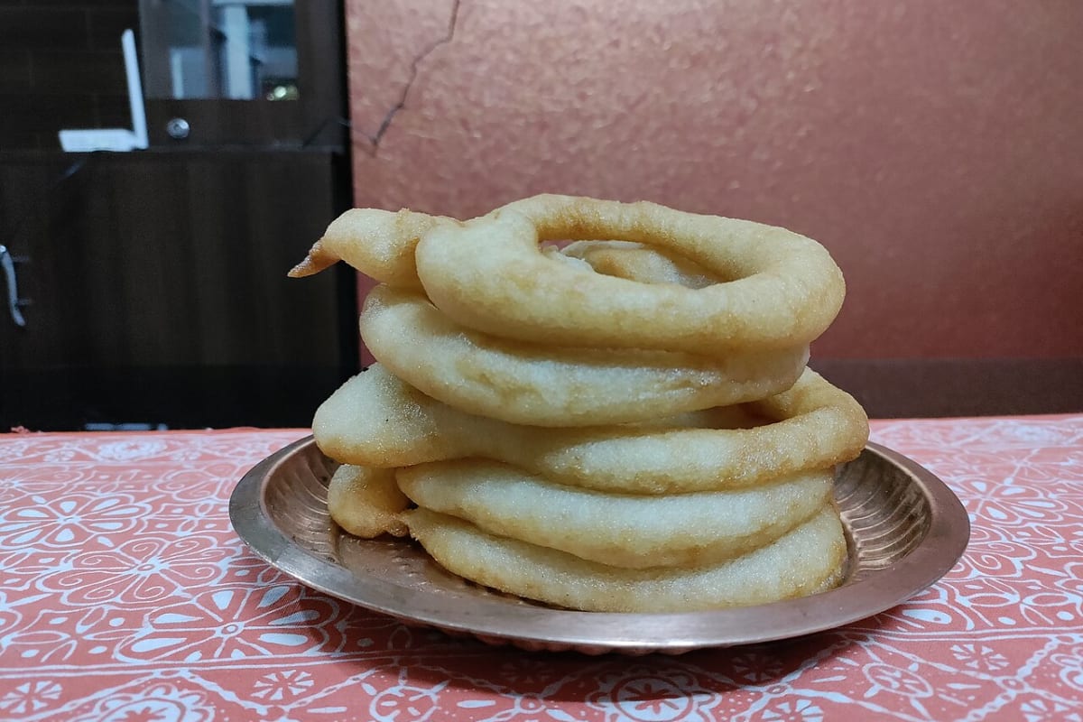 A stack of sel roti, ring-shaped fried rice-flour bread, on a metal plate.