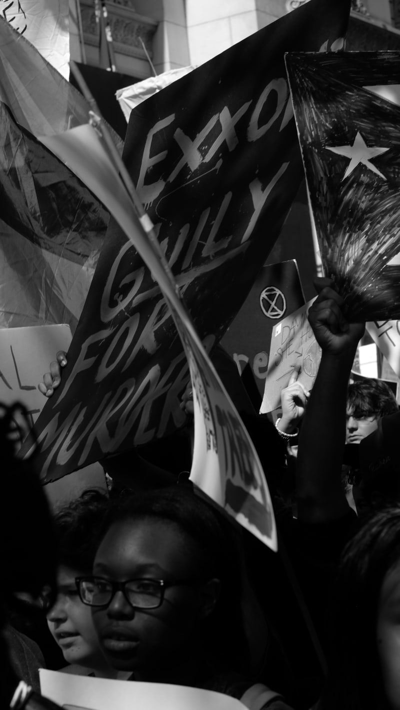“Exxon guilty for murder” – Concerned young faces shaded by protest signs held aloft