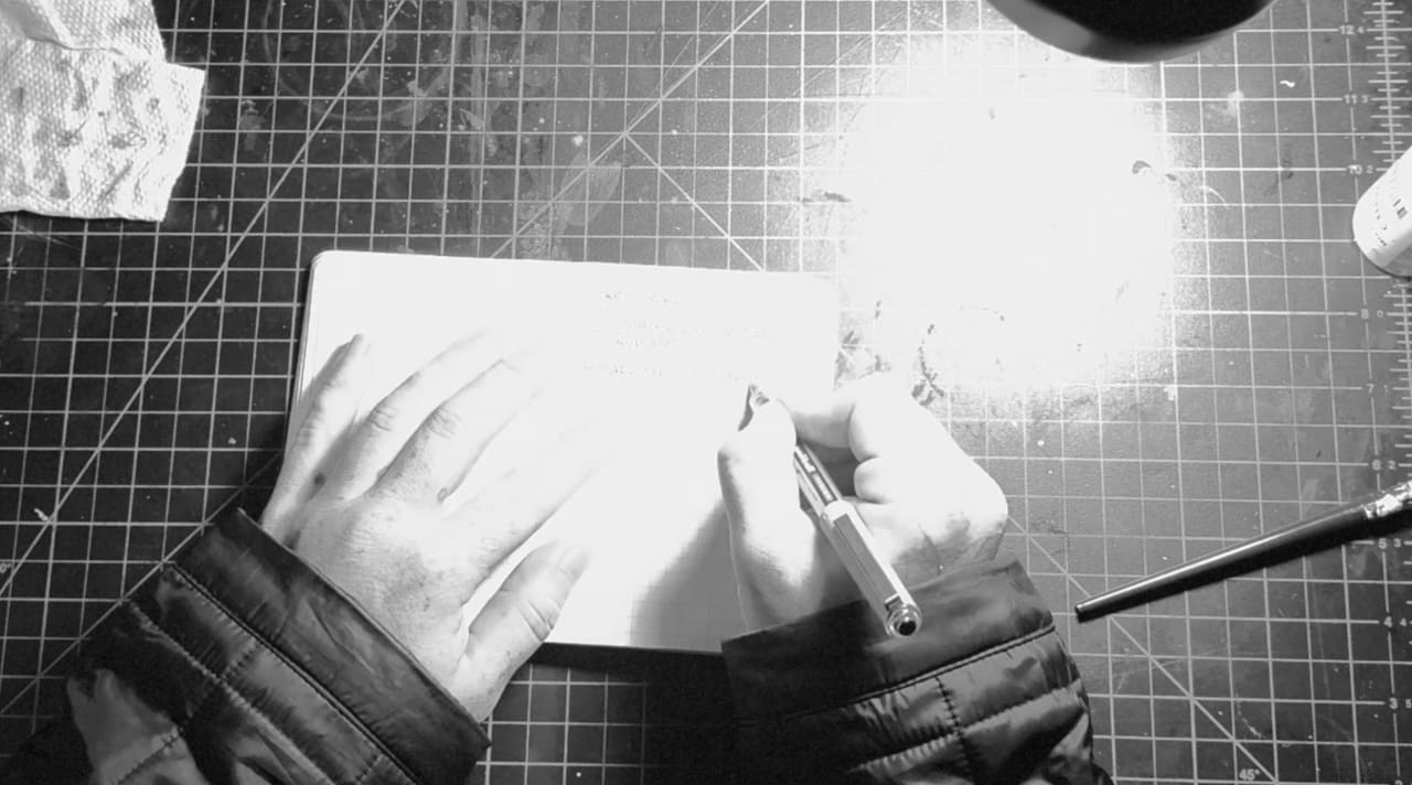 Artist's hands holding a paintbrush over a blank white canvas on a cutting mat, preparing to begin painting.