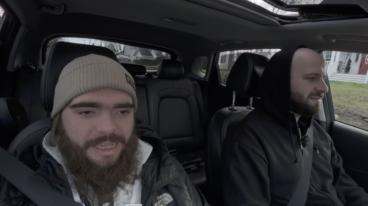 Two men in winter clothing sitting in a car's front seats during daytime.
