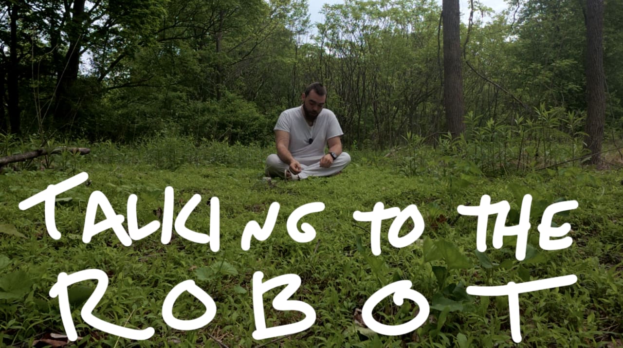 Man crouching in overgrown forest discussing robot technology, with text overlay reading 'TALKING TO THE ROBOT'