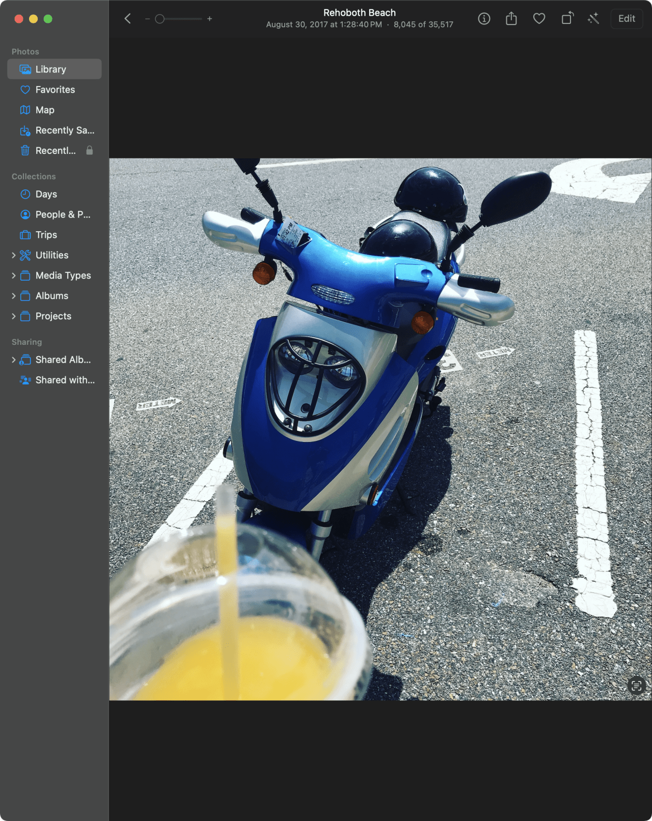 Blue and white scooter parked on asphalt with white parking lines at Rehoboth Beach, with a drink cup in foreground.