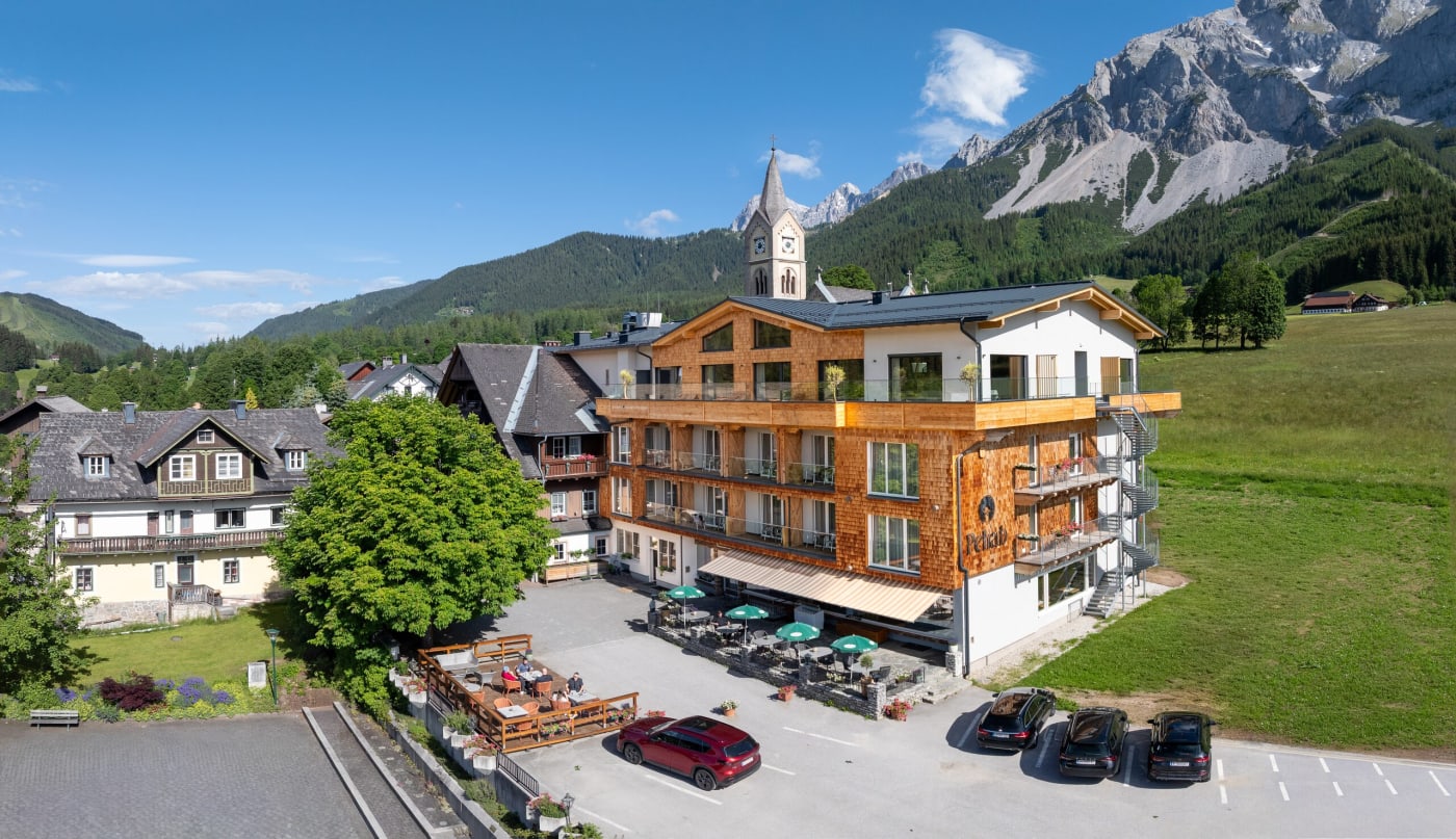 O hotel Pehab, a igreja e os prados de Ramsau am Dachstein, com o paredão do Dachstein ao fundo