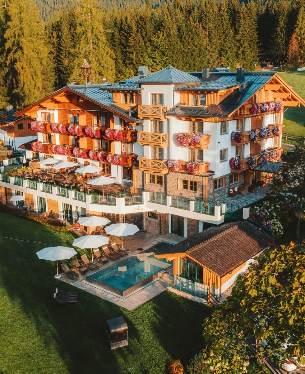 Vista aérea do hotel Lindenhof, de suas varandas floridas e da piscina externa, em Ramsau