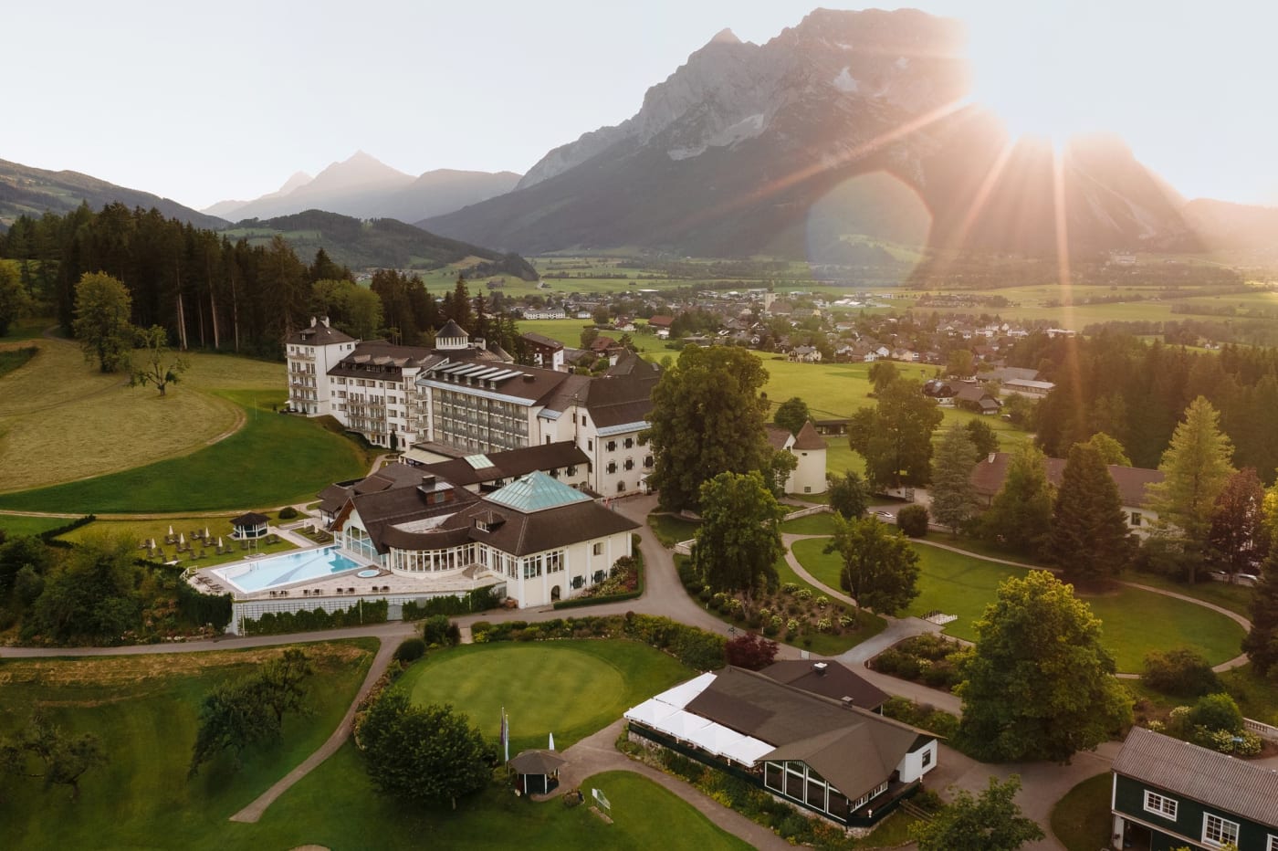Vista aérea do Schloss Pichlarn, de seu campo de golfe e da piscina ao pôr do sol, diante do maciço do Grimming