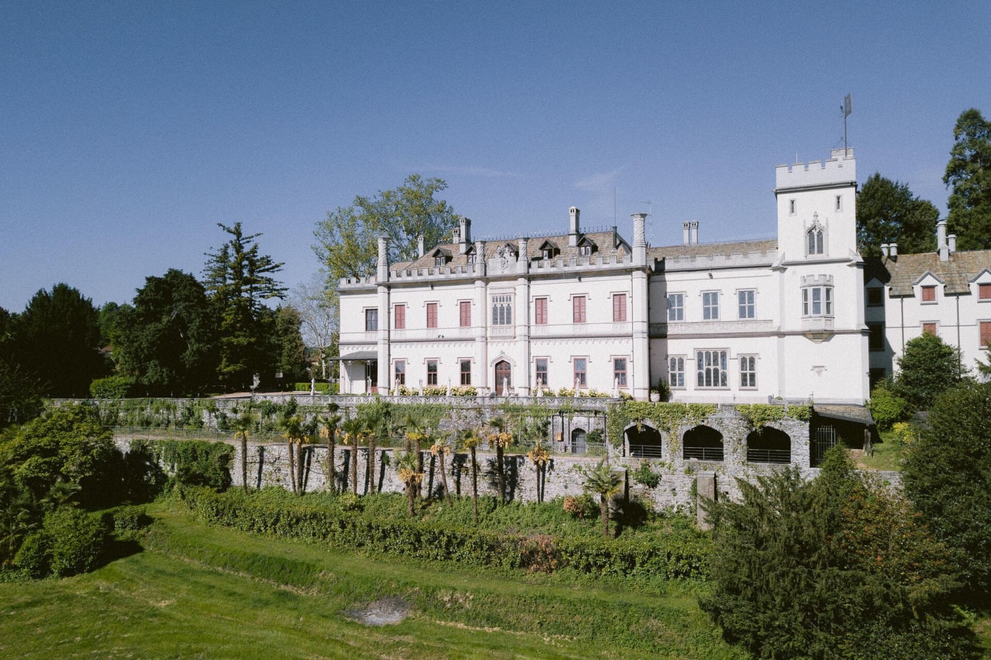El Castello Dal Pozzo, su fachada blanca y su torre, sobre sus terrazas cerca del lago Maggiore
