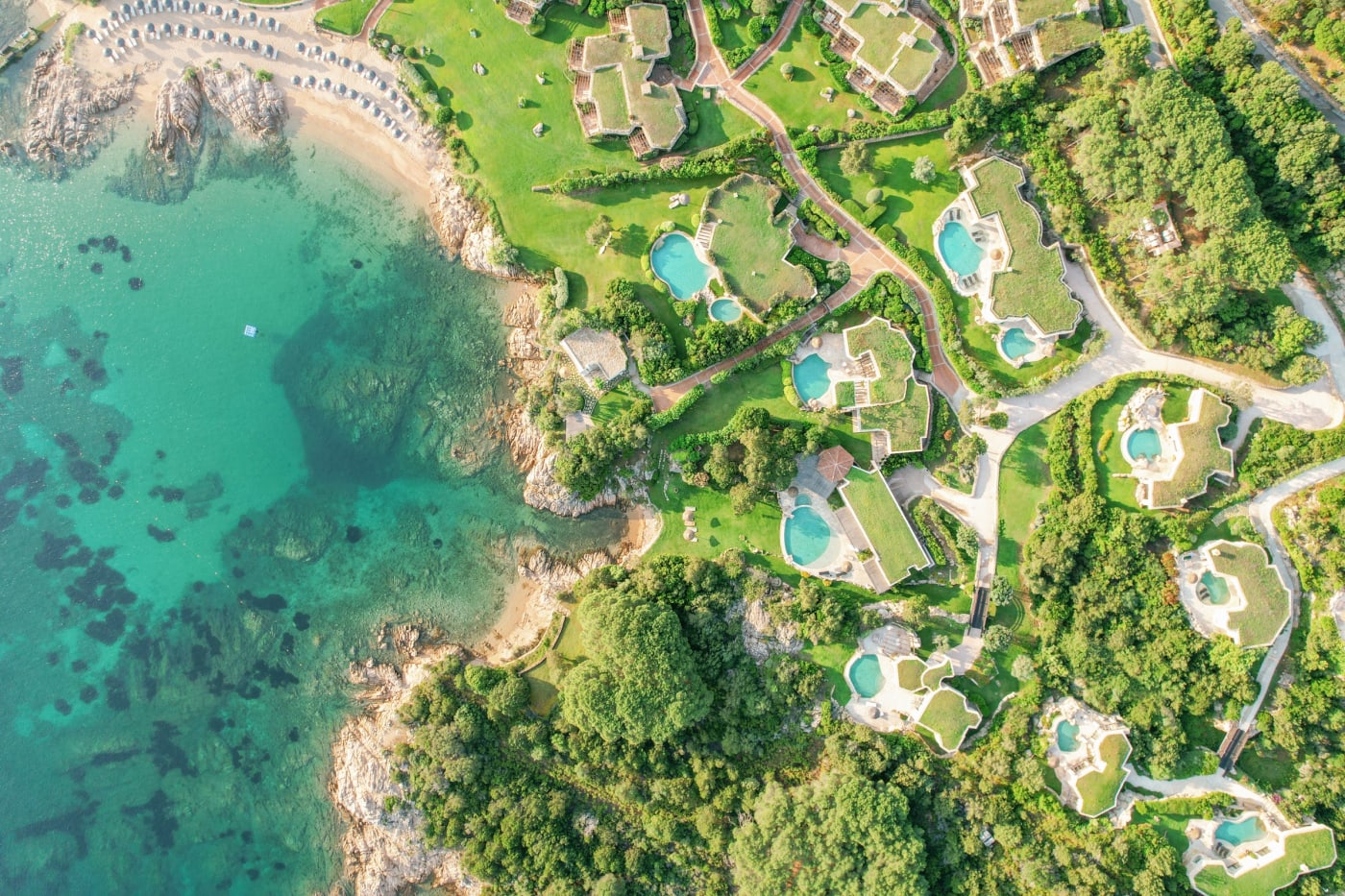 Luftaufnahme des Hotel Pitrizza: Villen mit Grasdächern und private Pools über einer türkisfarbenen Bucht auf Sardinien