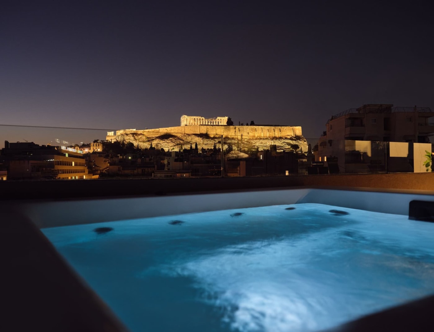 Jacuzzi éclairé du penthouse The Caryat à Koukaki, face à l'Acropole illuminée la nuit