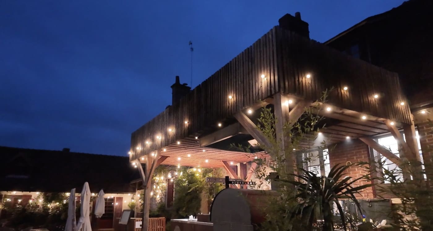 Die Terrasse des Restaurants Ardent im Loire Valley Lodges bei Einbruch der Nacht, Holzvordach mit Lichterketten und Außenküche