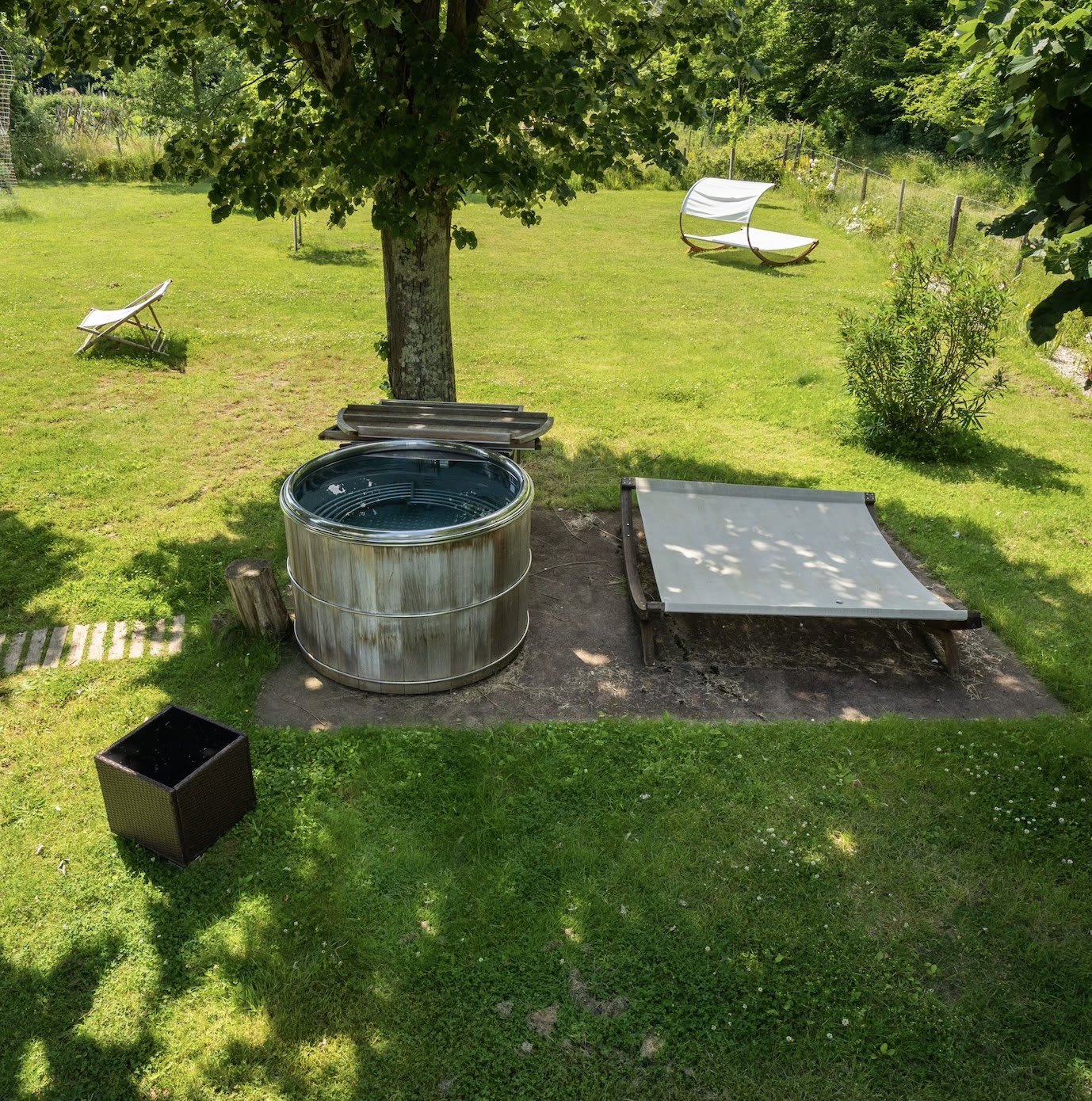 Das hölzerne Nordic Bath des Loire Valley Lodges auf dem Rasen, im Schatten eines Baumes, nahe dem Becken