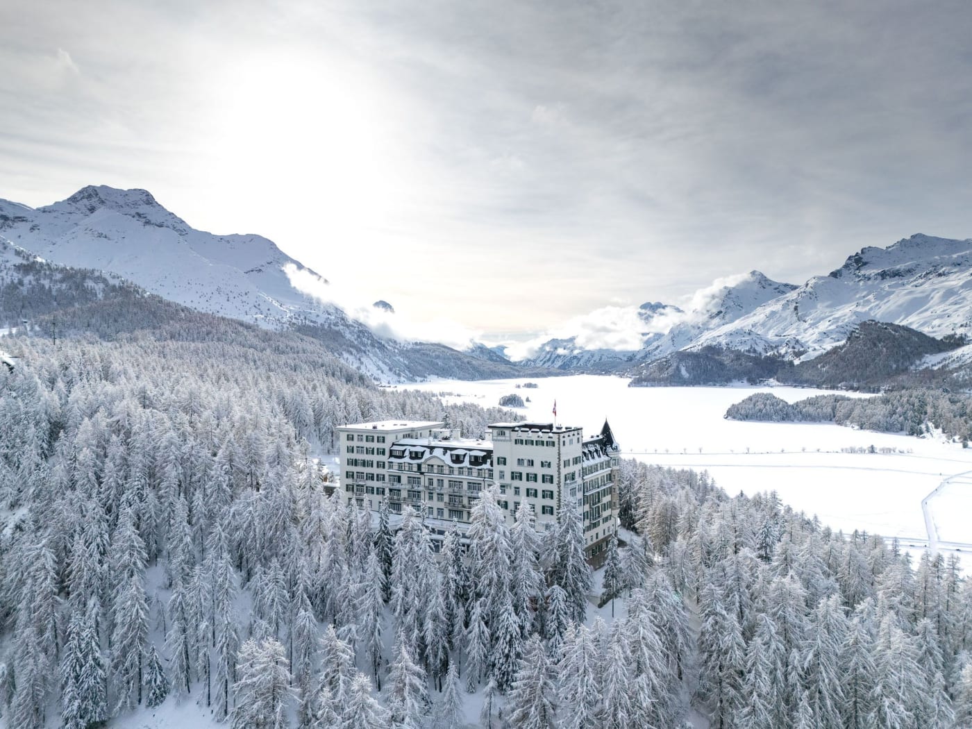 Vue aérienne de l'Hotel Waldhaus Sils dans la forêt enneigée, au-dessus du lac de Sils gelé