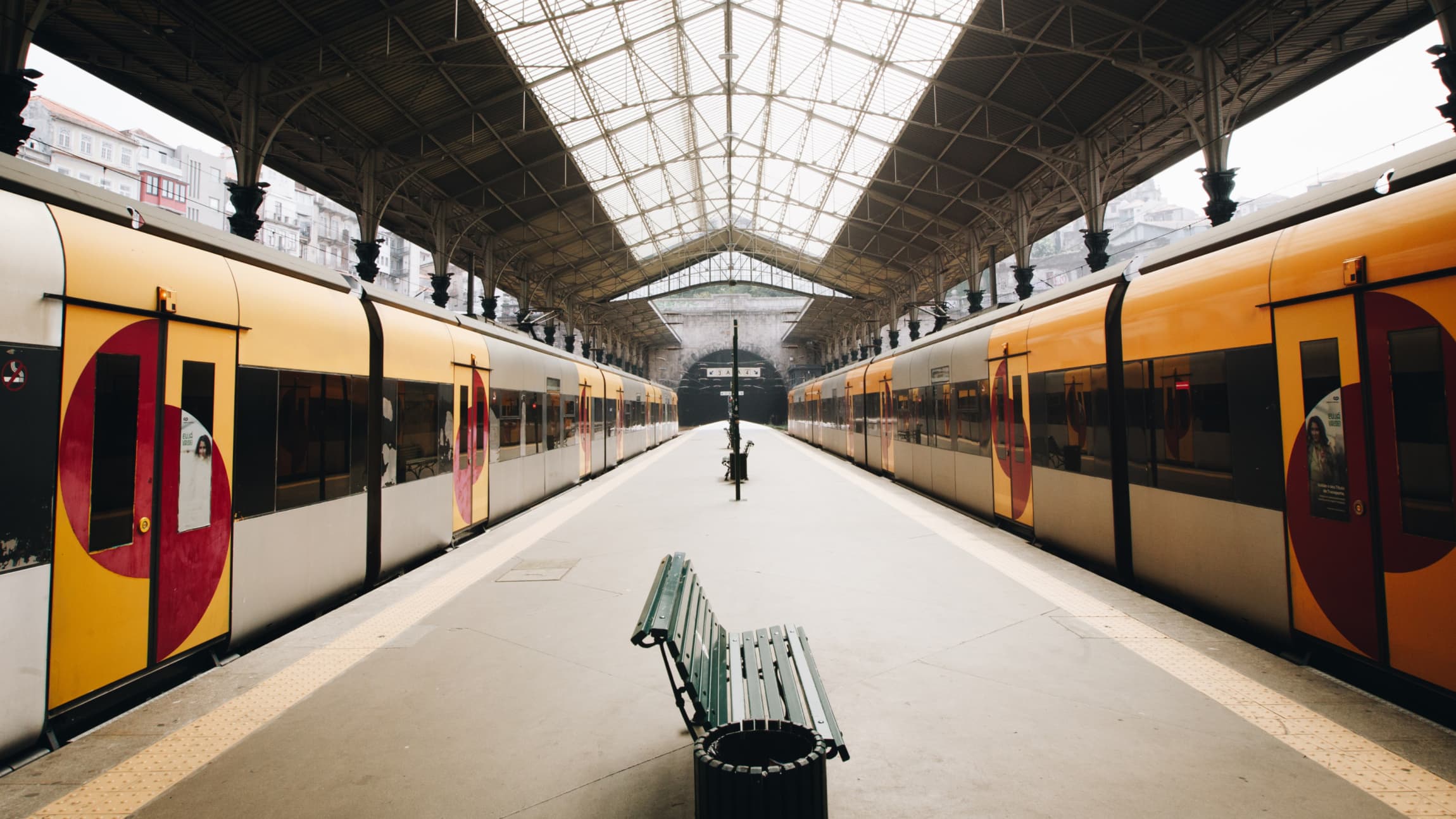 Long view of a train terminal between two parked trains with a green bench in the foreground.