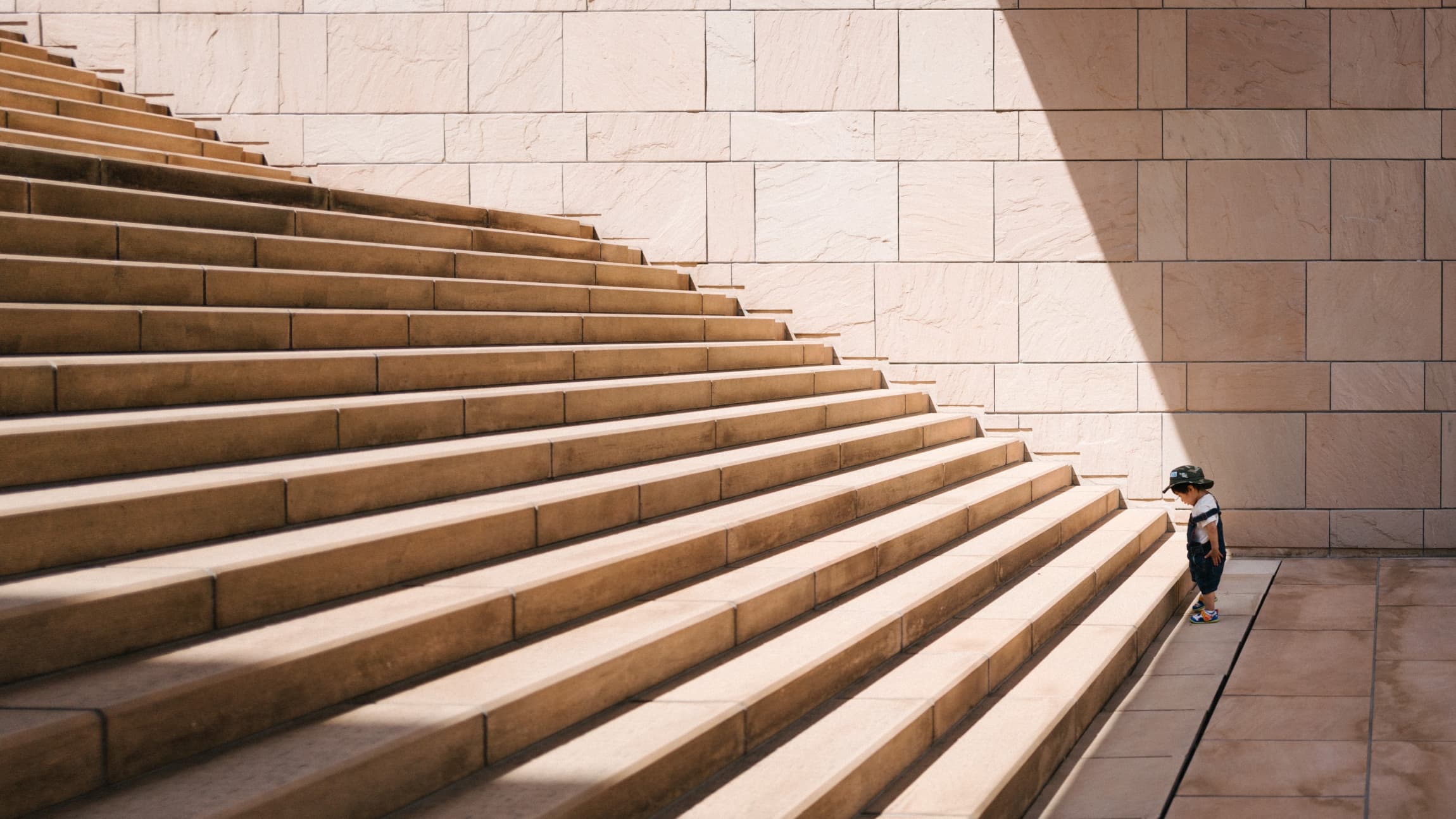 Small child looking down at a very large set of stairs to climb.