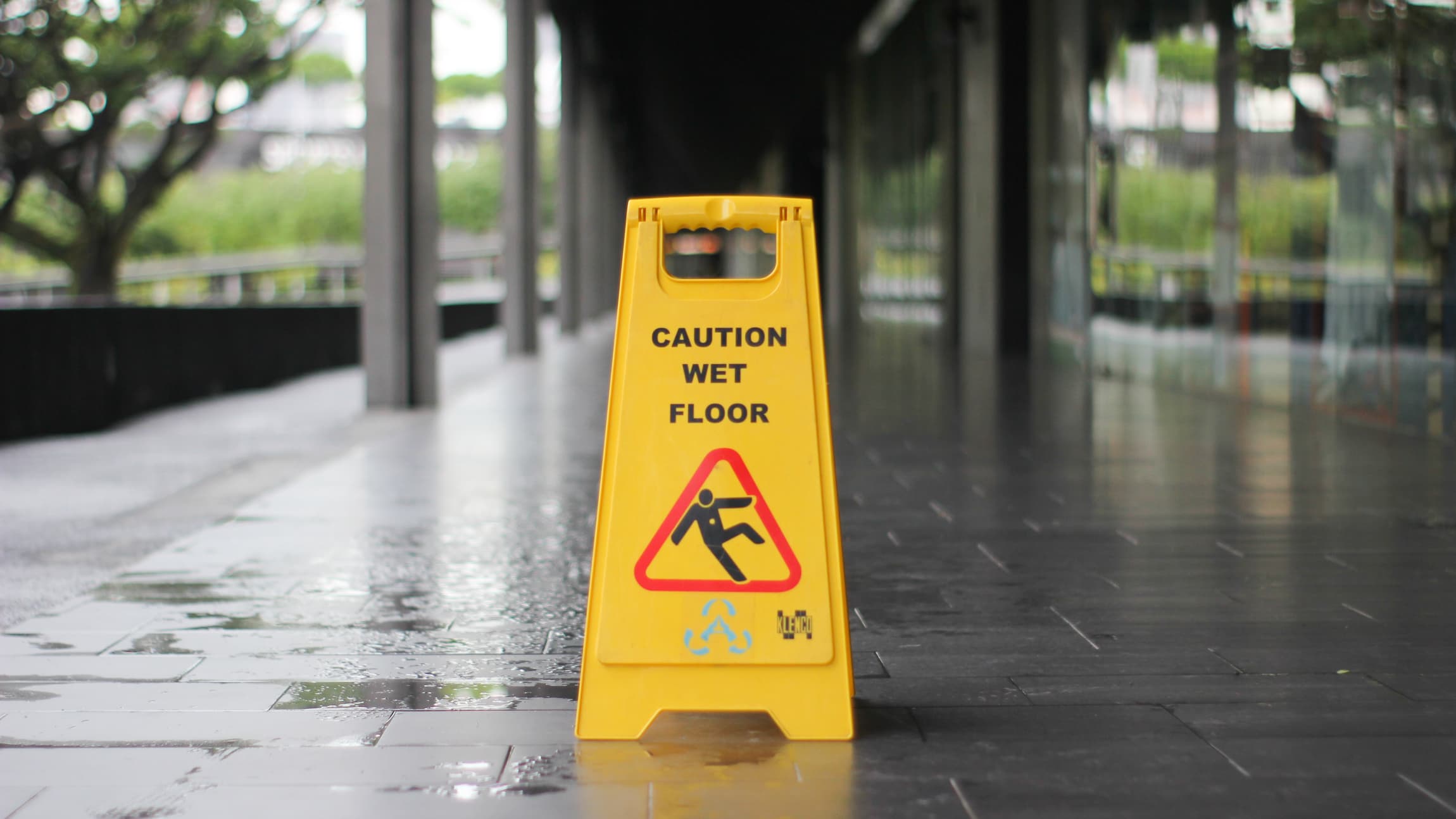 A yellow caution wet floor sign outside on a wet sidewalk.