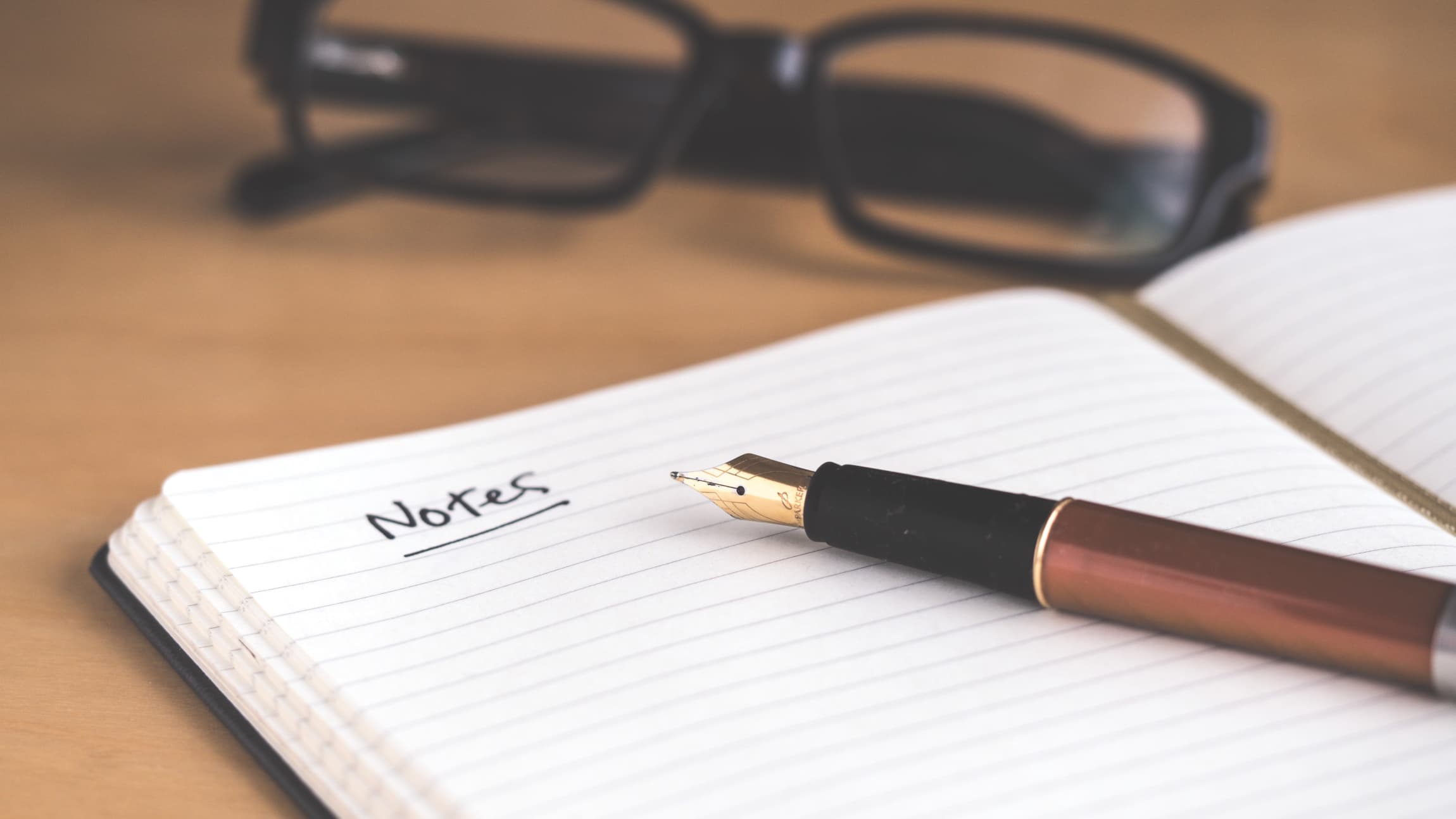 A notebook lies open on a desk with the word "Notes" written in it. 