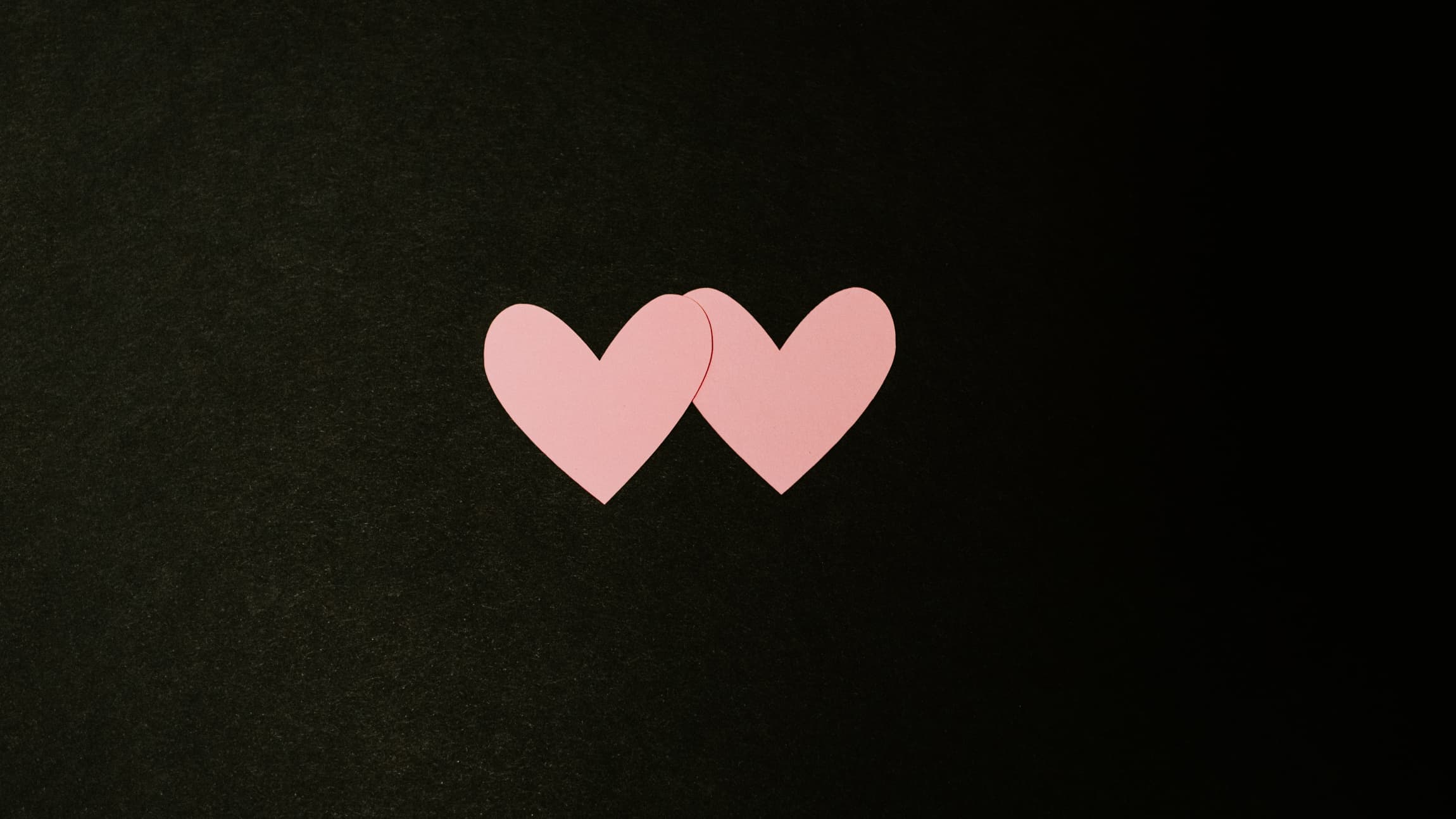 Black background with two pink hearts next to each other. 