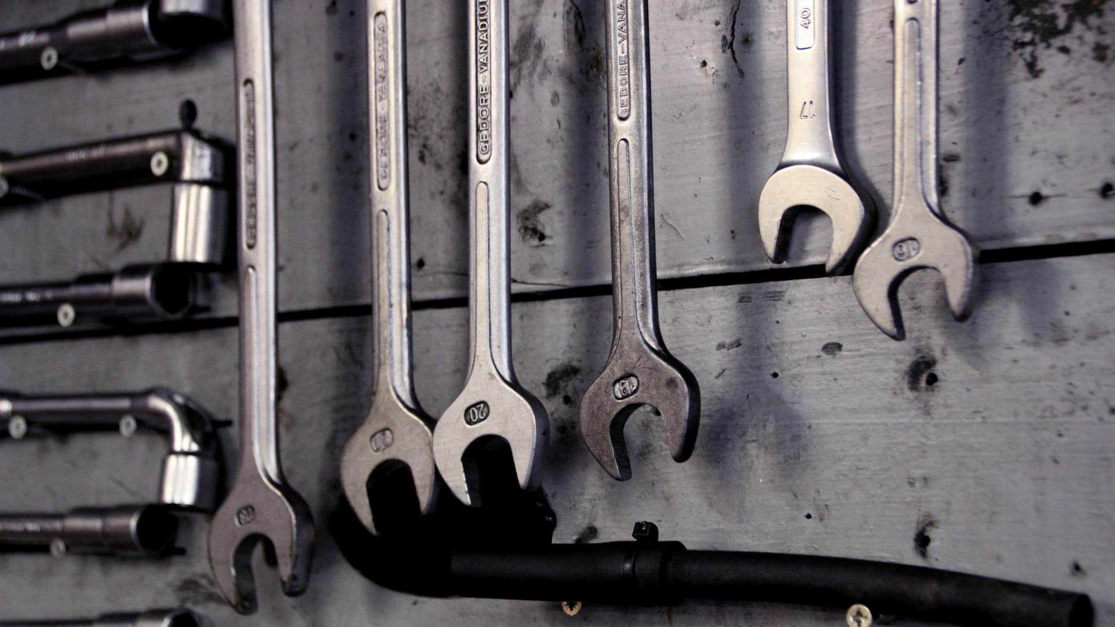 A monochromatic photo of a workbench with multiple wrenches hanging from the wall. 